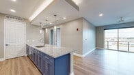 Located at 6842 Main St in Buffalo, NY, this well-appointed single-floor residence offers four bedrooms and two bathrooms with a thoughtfully designed layout. The open-concept kitchen and living area serves as the heart of the home, showcasing a striking large island with bold navy blue cabinetry, light granite countertops, and elegant pendant lighting overhead. White upper cabinets and stainless steel appliances, including a French door refrigerator and gas range, complete the kitchen's modern aesthetic. Light hardwood-style flooring runs throughout the main living areas, contributing to a clean, contemporary feel. The spacious primary bedroom stands out with floor-to-ceiling corner windows fitted with sleek roller shades, flooding the room with natural light and offering open views of the surrounding Buffalo neighborhood. Additional bedrooms feature plush carpeting and natural light from well-positioned windows. The bathrooms are finished with granite-topped white vanities, tall storage cabinetry, and matching hardwood-style flooring, maintaining a cohesive design language throughout. Neutral warm-gray walls provide a versatile backdrop across all rooms, while recessed lighting and large windows ensure the entire space feels bright and inviting.