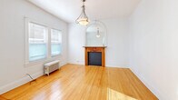 Located at 12467 Cedar Rd in Cleveland Heights, OH, this one-bedroom, one-bathroom unit offers a well-organized layout across a single floor, blending vintage architectural charm with functional living spaces. The living room serves as a standout centerpiece, showcasing warm hardwood floors, a decorative wood-mantled fireplace topped with an elegant arched mirror, a classic pendant light fixture, and a cast-iron radiator beneath double windows that fill the room with natural light. The bedroom is generously sized, continuing the hardwood flooring and featuring a ceiling fan, natural light from a window, a mirrored closet door, and a cast-iron radiator for supplemental heating. The kitchen offers ample white cabinetry, dark countertops, a tiled backsplash, white tile flooring, and a brass chandelier, equipped with a range and dishwasher. The bathroom is finished with marble-style tile floors, white subway tile walls, a soaking tub with shower, a rich wood vanity with a medicine cabinet mirror, a glass block window, and a cast-iron radiator. A connecting hallway links the rooms efficiently. Throughout, the crisp white walls and preserved hardwood floors create a bright, clean, and cohesive aesthetic rooted in classic residential architecture.