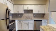 The Diamond floor plan is a single-story, one-bedroom, one-bathroom residence designed with a clean, modern aesthetic throughout. The kitchen serves as a standout feature, showcasing white shaker-style cabinetry with brushed nickel hardware, granite-look countertops, a gray subway tile backsplash, and a full suite of stainless steel appliances including a range, dishwasher, and refrigerator. Wood-look plank flooring runs through the kitchen and living areas, adding warmth and continuity to the space.

The open living area is generously proportioned, featuring neutral warm-gray walls, a textured ceiling, and a ceiling fan. Sliding glass doors lead to a private balcony, allowing natural light to fill the room and providing outdoor views. The bedroom is carpeted for comfort and benefits from multiple windows that bring in additional natural light.

The bathroom features wood-look plank flooring consistent with the rest of the unit, a white vanity with ample drawer storage, brushed nickel hardware, and a combined tub and shower. The overall design palette is cohesive and neutral, creating a bright, move-in-ready living environment.