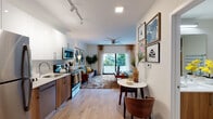 Located at 6320 SW Eighth St in West Miami, FL, this single-floor residence offers a thoughtfully designed open-plan layout that seamlessly connects the kitchen, dining, and living areas. Light wood-look tile flooring runs throughout, contributing to a bright and cohesive aesthetic.

The kitchen is outfitted with stainless steel appliances — including a full-size refrigerator, range, microwave, and dishwasher — complemented by two-tone cabinetry featuring crisp white upper cabinets and warm walnut-finish lower cabinets, set against light countertops. A compact dining area adjacent to the kitchen comfortably accommodates a small table and chairs. Track lighting overhead provides targeted illumination across the open living space.

The living area is generously proportioned, featuring a ceiling fan and an abundance of natural light streaming in through a large sliding glass door that opens onto a private balcony with outdoor views. The bedroom mirrors this layout with its own sliding glass door and balcony access, a ceiling fan, and ample room for furnishings.

The bathroom features a walnut-finish vanity with a white countertop, a large mirror, and a walk-in shower with tile surround. A louvered closet door provides convenient storage access nearby. The overall ambiance is modern, warm, and inviting — well-suited for comfortable urban living in the heart of West Miami.