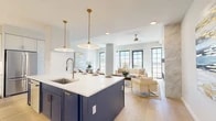 Located at 3111 Sunset Blvd in Flower Mound, TX, this contemporary three-floor home offers a thoughtfully designed layout across three well-proportioned levels. The main living floor showcases a stunning open-concept kitchen and living room bathed in natural light from large, black-framed grid windows. The kitchen features a bold navy blue island with white quartz countertops, gold-accented fixtures, elegant pendant lighting, and white upper cabinetry with stainless steel appliances. The adjoining living area includes light hardwood flooring, a sleek marble fireplace surround, and a ceiling fan, creating a warm yet refined atmosphere. Floor-to-ceiling windows on the upper level open to an outdoor balcony, further enhancing the sense of openness. The primary bedroom is a serene retreat complete with a ceiling fan and direct access to a spa-inspired en-suite bathroom featuring travertine tile flooring, a backlit vanity mirror, white cabinetry, and a glass-enclosed walk-in shower with full marble surround. A spacious walk-in closet with built-in shelving and hardwood flooring provides generous storage. Additional bathrooms echo the same refined aesthetic with marble tile and glass shower enclosures. The dedicated laundry room includes a full-size washer and dryer set on striking marble-look tile flooring, while five staircases connect the home's three levels seamlessly.
