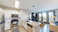 Located at 1000 Ashwood Pkwy in Atlanta, Georgia, this single-floor residence offers a well-designed layout with modern finishes throughout. The open-concept kitchen is a standout feature, appointed with white shaker cabinetry, subway tile backsplash, granite countertops, stainless steel appliances, and a central island with a built-in sink and pendant lighting overhead. The kitchen flows seamlessly into the living area, which is bright and inviting, benefiting from large windows and access to a private balcony that brings in generous natural light. A dedicated dining area with crown molding, wall sconces, and light wood-look flooring provides an elegant space for meals. The bedrooms offer a calm retreat, with carpeted floors and windows allowing natural light; one features a four-poster bed frame and a serene outdoor view. The bathroom includes a full tub-shower combination with clean white tile surround and oil-rubbed bronze fixtures. A conveniently located in-unit laundry closet houses a full-sized washer and dryer. Throughout the space, a neutral color palette, light hardwood-style flooring in the main areas, and thoughtful lighting create a cohesive and comfortable living environment.
