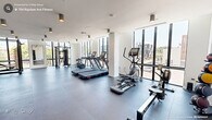 Located at 704 Rigsbee Ave in Durham, NC, this modern fitness center offers a well-appointed, single-floor workout space designed for a comprehensive exercise experience. The gym features a clean, contemporary aesthetic with crisp white walls, smooth high ceilings adorned with cylindrical pendant lighting, and durable dark rubberized flooring that spans the entire area.

Large floor-to-ceiling windows line the perimeter, flooding the space with abundant natural light and providing open views of the surrounding Durham streetscape. The bright, airy atmosphere enhances the overall workout environment, making the space feel expansive and inviting.

The fitness center is thoroughly equipped for both cardio and strength training. Cardio offerings include treadmills, an elliptical trainer, a stationary bike, and a rowing machine. Strength training equipment includes a multi-functional cable/smith machine rack, a dumbbell rack with a full range of free weights, adjustable benches, and plyometric boxes for functional training. A wall-mounted mirror provides visual feedback during workouts.

The layout is thoughtfully organized to maximize open floor space while keeping equipment accessible. The combination of modern equipment, generous natural light, and a clean design makes this fitness center a functional and motivating environment for residents or members in the heart of Durham.