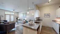 Located at 4986 Wetland Crossing in North Charleston, SC, this single-floor residence offers a thoughtfully designed open-concept layout that seamlessly connects the kitchen, dining, and living areas. The kitchen is a standout feature, equipped with stainless steel appliances, white cabinetry, granite countertops, and a central island with bar seating, all illuminated by stylish pendant lighting. Rich hardwood-style flooring runs throughout the main living areas, adding warmth and cohesion to the space. The living room is bright and inviting, benefiting from natural light streaming through large French doors with transom windows above, which open to the outdoors. The bedroom is carpeted for comfort and features generous windows that allow ample natural light, complemented by a ceiling fan. The bathroom is finished with granite countertops, white cabinetry, and a well-lit vanity with a large mirror. Throughout the residence, neutral tones and clean lines create a modern yet welcoming ambiance, making it a functional and attractive living space in the heart of North Charleston.