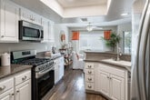 Located in Aliso Viejo, CA, this multi-level home spans three floors and offers a thoughtfully designed layout across generously proportioned living spaces. The entry level houses an attached garage with a dedicated laundry area tucked neatly beneath the staircase, complete with side-by-side washer and dryer and built-in shelving for storage. The main living floor features an open-concept arrangement combining the living room, dining area, and kitchen. The living room is bright and welcoming, with wood-look flooring, plantation shutters, and a cozy fireplace. The kitchen is well-equipped with white cabinetry, granite countertops, stainless steel appliances, a built-in pantry, and a breakfast bar with seating. The adjacent dining area benefits from natural light and a ceiling fan overhead. The upper floor is home to two bedrooms, including a spacious primary suite featuring vaulted ceilings, a warm accent wall, hardwood-style flooring, and floor-to-ceiling mirrored closet doors. The en-suite bathroom offers a walk-in shower and an extended vanity. A second full bathroom with a sliding glass tub-shower enclosure serves the additional bedroom. With six bathrooms total distributed across all three floors, the home ensures exceptional convenience throughout.