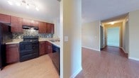 This single-floor residence offers a thoughtfully designed layout that balances comfort and functionality throughout. The kitchen is a standout feature, showcasing rich dark-wood cabinetry with sleek hardware, a mosaic tile backsplash, light stone-toned countertops, and a full suite of black appliances including an electric range, refrigerator, and dishwasher. Track lighting illuminates the space, and the kitchen opens seamlessly toward the main living area via a half-wall pass-through, enhancing the open feel.

The living and dining areas are expansive and bright, finished with warm hardwood-style flooring that extends throughout the main spaces. A decorative globe pendant light and ceiling fan add character, while vertical blinds on a large window allow natural light to filter in. A closet provides convenient in-unit storage just off the main living space.

The bedroom is generously proportioned, featuring plush neutral carpeting, a ceiling fan, a walk-in closet, and direct access to a bathroom. The bathroom is clean and functional, with a rich wood vanity, stone-toned countertop, a well-lit mirror, and wood-look flooring. A dedicated laundry room houses a full-size washer and dryer with overhead wire shelving for added storage. Textured ceilings and clean white trim are consistent throughout the home.