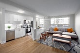 This thoughtfully designed one-bedroom, one-bathroom unit at 2293 Eglinton Ave E offers a clean, contemporary aesthetic throughout its efficiently laid-out single floor. Light oak-toned laminate flooring runs continuously across all areas, lending a cohesive, modern feel to the space.

The open-concept kitchen and living area forms the heart of the unit. The kitchen is outfitted with crisp white shaker-style cabinetry, white quartz countertops, subway tile backsplash, and a full suite of stainless steel appliances, including a refrigerator, electric range, and over-the-range microwave. A peninsula provides additional counter space and casual seating. A large window allows natural light to filter into the kitchen area.

The living room is generously proportioned for the overall footprint, featuring a wide window that frames outdoor views and fills the room with daylight. A wall-mounted mini-split unit provides climate control.

The bedroom is a comfortable, well-lit retreat with a sizeable window offering natural light and outdoor views. It includes a wall-mounted mini-split unit for individualized climate control.

The bathroom features a soaking tub with tiled surround and a clean white vanity. Neutral tones throughout the unit create a calm, inviting atmosphere well-suited for everyday living.