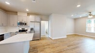 Located in Conroe, Texas, this single-story home offers a thoughtfully designed layout with three bedrooms, two bathrooms, and a patio — all finished with modern, cohesive details throughout. Light wood-look flooring runs continuously across the home, complemented by neutral gray-toned walls, white trim, and recessed lighting that creates a bright and clean aesthetic.

The open-concept kitchen is a standout feature, showcasing gray shaker cabinets, quartz countertops with a marble-like finish, a subway tile backsplash, and a center island with seating potential. Stainless steel appliances — including a refrigerator with ice maker, range, microwave, and dishwasher — complete the space. A door from the kitchen provides direct access to the patio and backyard.

The living room is generously sized with large windows allowing abundant natural light and a ceiling fan overhead. Each bedroom continues the warm flooring and neutral palette, with the primary bedroom featuring an en-suite bathroom equipped with a glass-enclosed shower and a gray vanity. The second bathroom includes a full tub-shower combo, a window for natural light, and matching vanity finishes.

A dedicated laundry room with built-in shelving and seven closets throughout provide ample storage. The backyard features a lush lawn and privacy fencing, offering a comfortable outdoor retreat.