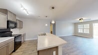 Located at 5210 Ballington Cir in Raleigh, NC, this single-floor, 4-bedroom, 2-bathroom home offers a well-designed layout with modern finishes throughout. The open-concept kitchen is a central highlight, featuring a large island with a built-in sink, light stone countertops, gray cabinetry, black appliances including a range and built-in microwave, and track lighting with crown molding accents. The kitchen flows seamlessly into the living room, which is brightened by natural light and provides direct access to a private balcony through a glass door. The living area is finished with hardwood-style flooring and a ceiling fan. The four bedrooms are generously proportioned, with the spacious primary bedroom offering plush carpeting, a ceiling fan, and an en-suite bathroom. The additional bedrooms also feature carpet flooring and ceiling fans. The two bathrooms include a shower-tub combo with chrome fixtures and hardwood-style flooring. A dedicated laundry room with washer/dryer hookups and a pet door adds everyday convenience. Neutral tones, clean trim work, and consistent finishes create a cohesive and move-in-ready atmosphere throughout the home.