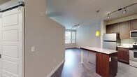 This well-appointed single-floor residence offers a thoughtfully designed layout that balances modern aesthetics with functional living. The open-concept kitchen is a standout feature, showcasing rich dark-wood cabinetry that extends to the ceiling, stainless steel appliances including a refrigerator, range, microwave, and dishwasher, a subway tile backsplash, and a granite-topped island with warm pendant lighting overhead. Track lighting further illuminates the space, adding a contemporary touch.

The living and dining area flows seamlessly from the kitchen, featuring dark hardwood-style flooring and a wall of windows fitted with horizontal blinds that invite generous natural light. A private exterior door with sidelight windows provides direct outdoor access, enhancing connectivity to the outside.

The bedrooms offer plush carpeting underfoot, each benefiting from natural light through blinds-fitted windows with views of surrounding greenery. One bedroom features a ceiling fan for added comfort. The bathroom is clean and functional, equipped with a soaking tub and shower combination, wood-style vinyl flooring, and neutral wall tones. Throughout the residence, soft neutral paint, clean white baseboards, and consistent finishes create a cohesive and inviting atmosphere.