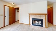 This single-floor unit offers a functional, well-organized layout with a neutral color palette of cream walls, warm wood trim, and light carpet throughout the living and sleeping areas. The spacious living room is a standout feature, anchored by a large picture window that admits generous natural light and offers outdoor views. Flush-mount lighting illuminates the space, and a textured popcorn ceiling is consistent throughout. A pass-through window connects the living area to the kitchen, enhancing the open feel between spaces.

The galley-style kitchen is efficiently designed, featuring warm wood cabinetry extending to the upper walls for ample storage, laminate countertops, a double sink, and white appliances including a refrigerator, range, and dishwasher. Light vinyl flooring adds practicality to the kitchen. A door at the end of the kitchen provides additional access to the unit.

The bedrooms are carpeted and well-proportioned, with one room featuring a window that brings in natural light. The bathroom includes a single-basin vanity with a large wall mirror, tile-style countertop, and a tub-shower combination. Wood-tone doors and trim are consistent throughout, contributing to a cohesive and clean interior aesthetic.