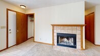 This single-floor unit offers a functional, well-organized layout with a neutral color palette of cream walls, warm wood trim, and light carpet throughout the living and sleeping areas. The spacious living room is a standout feature, anchored by a large picture window that admits generous natural light and offers outdoor views. Flush-mount lighting illuminates the space, and a textured popcorn ceiling is consistent throughout. A pass-through window connects the living area to the kitchen, enhancing the open feel between spaces.

The galley-style kitchen is efficiently designed, featuring warm wood cabinetry extending to the upper walls for ample storage, laminate countertops, a double sink, and white appliances including a refrigerator, range, and dishwasher. Light vinyl flooring adds practicality to the kitchen. A door at the end of the kitchen provides additional access to the unit.

The bedrooms are carpeted and well-proportioned, with one room featuring a window that brings in natural light. The bathroom includes a single-basin vanity with a large wall mirror, tile-style countertop, and a tub-shower combination. Wood-tone doors and trim are consistent throughout, contributing to a cohesive and clean interior aesthetic.
