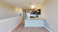 Located at 2925 Countrywood Parkway in Memphis, TN, this single-floor unit offers a thoughtfully designed open-concept layout that maximizes every inch of its compact footprint. The combined kitchen and living area serves as the heart of the space, where contemporary dark espresso cabinetry contrasts beautifully with granite countertops and a white subway tile backsplash. Stainless steel appliances, including a range, microwave, and dishwasher, lend a polished, modern feel to the kitchen. A peninsula with a stainless steel sink doubles as a breakfast bar, providing a natural division between the cooking and living zones. Pendant lighting above the peninsula and track lighting overhead add layered illumination throughout. Light wood-tone flooring runs seamlessly across the entire living area, enhancing the sense of openness. The living room benefits from large, multi-pane windows with exterior views, while a ceiling fan ensures year-round comfort. The bathroom is clean and functional, featuring a full tub-shower combo with a white surround, granite-topped vanity, and matching light flooring. Neutral warm-gray walls throughout create a cohesive, move-in-ready aesthetic ideal for comfortable urban living.