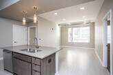 This single-floor unit showcases a thoughtfully designed open-concept layout that seamlessly connects the kitchen and living area. The kitchen serves as a central focal point, featuring a large island with a double basin sink, quartz-style countertops, rich dark wood cabinetry extending to the ceiling, and a full suite of stainless steel appliances including a French door refrigerator, range, and dishwasher. Pendant lighting and a decorative geometric-patterned ceiling accent add visual interest above the island. Exposed industrial-style ductwork runs through the kitchen and bedroom areas, lending a modern, loft-inspired character to the space. Light tile flooring flows throughout the main living areas, while the bedroom features plush carpeting and a spacious walk-in closet with wire shelving. The living area benefits from natural light through large windows with blinds. Two bathrooms are finished with light tile flooring, soaking tubs with shower combinations, and dark wood cabinetry for storage. A dedicated in-unit laundry closet houses a full-size front-loading washer and dryer with overhead shelving, adding everyday practicality to this well-appointed home.
