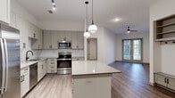 This single-floor, 2-bedroom, 2-bathroom unit offers a well-designed open-concept layout connecting the kitchen and living area. The kitchen is a standout feature, equipped with stainless steel appliances including a French door refrigerator, electric range, and built-in microwave. Gray-toned shaker-style cabinetry with matte black hardware pairs with a subway tile backsplash and light quartz countertops. A large center island with pendant lighting above serves as both a prep space and a natural dividing point between the kitchen and living area. The living room benefits from natural light through glass French doors and is finished with wood-look flooring that extends throughout the unit, creating a cohesive aesthetic.

The bedrooms are well-proportioned, with the primary bedroom offering comfortable dimensions and access to a closet with built-in shelving and hanging rods. Both bathrooms feature shaker-style vanities, matte black fixtures, and large framed mirrors. A dedicated laundry room accommodates a full-size washer. Clean white walls, consistent wood-look flooring, and modern fixtures contribute to a cohesive, contemporary ambiance throughout the unit.
