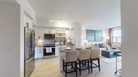 Located at 3991 NW 82nd Dr in Cooper City, Florida, this single-story residence showcases a thoughtfully designed open-concept layout that seamlessly connects the kitchen, dining, and living areas. The kitchen is a standout feature, outfitted with white shaker cabinetry accented by matte black hardware, a herringbone-patterned tile backsplash, stainless steel appliances including a French door refrigerator and gas range, and a large central island with a gray quartz countertop that doubles as a casual dining bar. Pendant lighting and track lighting illuminate the space with a warm, contemporary glow. Light wood-look flooring runs throughout, enhancing the bright and airy atmosphere. The living room is generously proportioned, featuring a ceiling fan, large windows, and glass door access to an outdoor area with lush greenery and palm trees. The bedroom offers a serene retreat with warm lighting, windows dressed in rich brown drapes, and peaceful views. The bathroom is finished with white cabinetry, a white quartz vanity, matte black fixtures, wood-look tile flooring, and a glass-enclosed shower. Clean white walls and modern finishes throughout give this residence a polished, move-in-ready appeal.