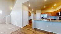 This two-story home is designed with a practical and cohesive aesthetic, combining warm tones and durable finishes throughout. The main level centers around an open-concept kitchen and living area, where rich hardwood-style flooring flows seamlessly underfoot. The kitchen is well-appointed with warm wood cabinetry extending to the upper walls, granite-style countertops, and a full suite of stainless steel appliances including a refrigerator with an in-door dispenser, an electric range, a built-in microwave, and a dishwasher. A peninsula with a raised granite countertop bar provides additional prep space and casual seating. Recessed lighting illuminates the kitchen, complementing the natural light that filters in through the windows. The adjoining living area transitions to plush carpet, creating a comfortable, defined space.

The bedrooms are carpeted and bathed in natural light through sizable windows fitted with blinds. The primary bathroom offers a dual-sink vanity with granite countertops, warm wood cabinetry, hardwood-style flooring, and a separate shower area. A secondary bathroom features a full tub-shower combo and a single vanity. A generously sized walk-in closet with multi-tiered wire shelving and hanging rods provides substantial storage capacity.