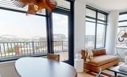 This contemporary 750 square foot apartment in Washington, DC offers a harmonious blend of style and functionality. The open-concept living area features light wood flooring and expansive windows that flood the space with natural light, providing breathtaking views of the city skyline, including prominent landmarks.

The living room is thoughtfully furnished with a mix of modern and mid-century pieces, including a plush orange sofa and a cozy white armchair. A striking wooden pendant light and artistic wall hangings add visual interest and warmth to the space.

The dining area seamlessly connects to the living room, showcasing a wooden table with mixed seating options. A unique wooden light fixture overhead complements the overall aesthetic.

The primary bedroom, measuring 140 square feet, boasts a king-sized bed with pink linens and built-in closets for ample storage. The bathrooms feature sleek, modern designs with dark tile work, glass shower enclosures, and floating vanities.

Throughout the apartment, large windows with black frames offer panoramic city views, including a stadium visible from one of the bedrooms. The kitchen, while not fully visible in the images, appears to be integrated into the open living space.

This well-designed apartment maximizes its 750 square feet, creating a sophisticated urban retreat that balances style, comfort, and functionality in the heart of the nation's capital.