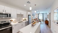 This well-appointed one-bedroom, one-bathroom residence in Surprise, AZ offers a thoughtfully designed layout that maximizes every square foot. Light-toned wood-look flooring flows throughout the main living areas, creating a cohesive and modern aesthetic.

The kitchen is a standout feature, showcasing crisp white cabinetry with matte black hardware, quartz countertops, a subway tile backsplash, and a full suite of stainless steel appliances including a refrigerator, range, microwave, and dishwasher. A central island with pendant lighting provides additional prep space and casual seating, making the kitchen as functional as it is visually appealing.

The open-concept living area is bathed in natural light from large windows dressed with sheer curtains, and is finished with a ceiling fan for year-round comfort. The space offers a relaxed, inviting ambiance well-suited for both everyday living and entertaining.

The bedroom is a comfortable retreat, featuring plush carpeting, a ceiling fan, generous natural light from a large window, and a dedicated closet for ample storage. The clean, neutral palette throughout the bedroom enhances its calm atmosphere.

Additional highlights include a private balcony and a well-designed bathroom. The overall design reflects a clean, contemporary style with quality finishes that define modern residential living.