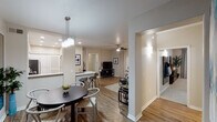 This single-floor residence offers a thoughtfully designed open-concept layout that seamlessly connects the main living areas. Wood-style flooring runs throughout the common spaces, providing a warm and cohesive aesthetic.

The kitchen is well-equipped with stainless steel appliances, including a gas range, over-the-range microwave, dishwasher, and refrigerator. Crisp white cabinetry with ample storage and light-toned countertops complete the functional and clean design. A breakfast bar with barstool seating bridges the kitchen to the dining area.

The dining space is anchored by a round table and a modern multi-pendant chandelier, with large mirror panels that reflect light and add depth to the room. It flows naturally into the living room, which features a ceiling fan, a patio door with decorative drapes and blinds allowing natural light, and a comfortable seating arrangement.

A welcoming hallway entrance, accented with wall art and sconce lighting, connects to the rest of the unit. Two bedrooms are appointed with plush carpet flooring, ceiling fans, and multiple windows with blinds. One bedroom features neutral tones and ample natural light, while the other is carpeted and well-lit.

Overall, the space presents a modern, neutral palette with consistent finishes throughout, creating a comfortable and livable environment.