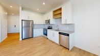 Located at 8643 Norris View Ln in West Jordan, Utah, this single-floor unit offers a clean, modern design with consistent light wood-style flooring and crisp white walls throughout. The open-concept layout creates a seamless flow between the living area and kitchen, with natural light streaming in through large windows complemented by a ceiling fan overhead.

The kitchen is a standout feature, outfitted with white shaker-style cabinetry, warm wood open shelving, and a classic subway tile backsplash. A full suite of stainless steel appliances includes a refrigerator, electric range, built-in microwave, and dishwasher. Neutral-toned countertops and an undermount sink complete the functional and stylish space.

The bathroom maintains the unit's clean aesthetic with a white vanity, integrated sink, large mirror, and a full tub-shower combination with built-in shelving. Light wood flooring carries through this space as well, reinforcing the cohesive design language.

The remaining rooms feature bright, open walls offering versatile use of space, with recessed lighting and easy access to a hallway with a louvered closet door for additional storage. The electrical panel is conveniently integrated into the layout. Overall, the unit presents a fresh, move-in-ready environment with a modern, minimalist character.