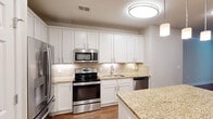 Located at 4203 Legacy Oaks Pl in Asheville, NC, this well-appointed single-floor residence offers two bedrooms, two bathrooms, and a thoughtfully designed layout across a comfortable footprint. The kitchen is a standout feature, showcasing crisp white shaker cabinetry, granite countertops, a tile backsplash, and a full suite of stainless steel appliances including a refrigerator, range, microwave, and dishwasher. A central island with pendant lighting above provides additional prep space and casual seating. Wood-look flooring runs throughout the main living and kitchen areas, adding warmth and cohesion. The spacious primary bedroom features crown molding, a ceiling fan, large windows with natural light, and direct access to a closet. The primary bathroom includes a granite-topped vanity, a walk-in shower, and a separate soaking tub. The second bedroom is carpeted with a ceiling fan and a window overlooking greenery. A second full bathroom mirrors the quality finishes found throughout the home. With seven closets total, storage is abundant. A dedicated laundry area adds everyday convenience, rounding out this functional and attractive Asheville residence.