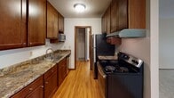 This single-floor unit at 175 McKnight Rd N in Saint Paul, Minnesota offers a functional and well-organized layout. The interior hallway serves as the central connector between spaces, featuring hardwood flooring, louvered storage closets, and warm wood-trimmed doorways throughout.

The galley-style kitchen is equipped with rich dark wood cabinetry, granite-look countertops, stainless steel appliances including a refrigerator and range with overhead ventilation, and a double basin sink. Hardwood flooring and a textured ceiling complete the kitchen's practical design. A walk-in pantry or storage closet is accessible directly from the kitchen.

The living area is generously sized with plush carpeting, neutral walls, and a sliding glass door that opens to an outdoor space with views of mature trees and greenery. A wall-mounted air conditioning unit and baseboard heating ensure year-round comfort. The open sightline to the kitchen adds to the spacious feel of the living space.

Bedrooms are carpeted and receive natural light through large windows overlooking wooded surroundings. Ceiling fans with light fixtures are present in the bedrooms. The bathroom features a single-basin vanity with dark wood cabinetry, a large wall mirror, and clean white countertops with brushed nickel fixtures.