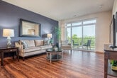 This thoughtfully designed one-bedroom, one-bathroom residence offers a comfortable and functional single-floor layout. The open-concept living area seamlessly connects the kitchen, dining, and living spaces, all unified by warm hardwood flooring throughout. The kitchen is a standout feature, showcasing rich wood cabinetry, granite countertops, a large center island with a double sink and bar seating, and a full suite of stainless steel appliances including a gas range and built-in microwave. Pendant lighting above the island adds a refined touch. The dining area flows naturally from the kitchen, while the living room is anchored by a bold accent wall and large sliding glass doors that flood the space with natural light and open onto a private balcony with scenic outdoor views. The bedroom features plush carpeting and direct access to a dedicated closet. The bathroom includes warm wood vanity cabinetry, a white quartz countertop, a large mirror, and a walk-in shower with safety grab bars. Throughout the residence, warm-toned wood trim, vaulted ceiling lines in the kitchen, and carefully considered color accents contribute to a welcoming and modern ambiance.