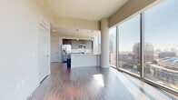 Located in the heart of Uptown Charlotte at 401 S. Graham Street, this high-rise unit offers a sleek, modern living experience defined by dramatic floor-to-ceiling glass walls that frame sweeping panoramic views of the Charlotte skyline, Bank of America Stadium, and the surrounding cityscape. Rich hardwood-style flooring flows throughout the open living and dining areas, reflecting abundant natural light that pours in throughout the day. The contemporary kitchen is thoughtfully designed with dark, flat-front cabinetry, white quartz countertops, a subway tile backsplash, stainless steel appliances including a French door refrigerator, and pendant lighting above the breakfast bar peninsula. The living area is an expansive, light-filled space anchored by corner floor-to-ceiling windows, creating an airy, open ambiance with unobstructed city views. The bedroom continues the floor-to-ceiling window theme, offering a serene retreat with more stunning vistas and direct access to a private balcony. The bathroom features large-format tile flooring, a dark wood vanity with quartz countertop, a walk-in shower, and clean, modern fixtures. Utility closets and ample storage options complete this well-appointed urban residence.