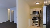 This single-floor residential space is thoughtfully laid out to maximize functionality and comfort. The kitchen is a standout feature, equipped with stainless steel appliances including a gas range, over-the-range microwave, and complemented by crisp white cabinetry that provides ample storage. A classic white subway tile backsplash adds a timeless aesthetic touch, while light granite-style countertops offer a practical and clean workspace. The kitchen is finished with light tile flooring, which contrasts neatly with the darker hardwood-style flooring found in the adjoining areas. Neutral, warm-toned walls throughout lend the space a bright and welcoming ambiance. A partial wall separates the kitchen from the rest of the unit, creating a sense of definition between spaces while maintaining an open feel. Adjacent to the kitchen, a hallway leads to additional rooms, including what appears to be a closeted space or bedroom, suggesting a well-organized and efficiently designed floor plan. Flush ceiling lighting provides consistent illumination throughout. Overall, the space offers a practical and clean living environment with a cohesive design aesthetic.