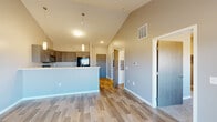 Located at 2300 N Valley View Rd in Sioux Falls, SD, this thoughtfully designed one-bedroom, one-bathroom unit offers a well-appointed layout across a single floor. The open-concept kitchen and living area is anchored by soaring vaulted ceilings that lend an expansive feel well beyond the unit's compact footprint. The kitchen is equipped with gray shaker-style cabinetry, light stone countertops, a peninsula with a sink, pendant lighting, and a full suite of black Whirlpool appliances including a refrigerator, range, and over-the-range microwave. Wood-look plank flooring extends throughout the main living area, which features a ceiling fan and sliding glass doors opening onto a private balcony with open prairie views. The bedroom offers plush carpet, a bright window with outdoor views, a walk-in closet, and direct access to the full bathroom. The bathroom includes a shaker-style vanity with stone countertop, a soaking tub with shower, and wood-look tile flooring. A dedicated laundry room houses a full-size Whirlpool washer and dryer with overhead shelving, complemented by a separate utility room for additional functionality. Neutral gray tones throughout create a clean, modern aesthetic.