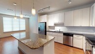 This single-floor residence offers a thoughtfully designed open-concept layout that seamlessly connects the kitchen and living areas. The kitchen is a standout feature, showcasing white shaker cabinetry, a full suite of stainless steel appliances including a French door refrigerator, dishwasher, range, and built-in microwave. A large granite-topped island with pendant lighting serves as both a functional workspace and a natural gathering point. Rich hardwood flooring runs throughout the main living and kitchen areas, complemented by track lighting overhead.

The living room is generous in scale, featuring large windows that invite abundant natural light and access to an outdoor area via glass doors. A ceiling fan adds both style and comfort to the space.

The bedrooms are carpeted for warmth and comfort, with large windows and ceiling fans. One bedroom includes a walk-in closet with built-in shelving. An additional room with hardwood flooring offers flexible use as a bedroom or office.

The bathroom is well-equipped with a soaking tub, separate glass-enclosed shower, extended vanity with dark granite countertop, white cabinetry, and clean tile flooring, creating a practical and polished finish throughout.