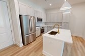 This 850-square-foot, one-bedroom, one-bathroom apartment at 5301 W Tyson Ave in Tampa, FL offers a well-designed single-floor layout with modern finishes throughout. The open-concept kitchen and living room serves as the heart of the unit, featuring a large center island with a white quartz countertop, a gold-accented sink, and stylish pendant lighting. The kitchen is outfitted with light gray shaker-style cabinetry, white subway tile backsplash, stainless steel appliances including a French door refrigerator, range, and built-in microwave, all complemented by light wood-tone flooring that extends throughout the unit. The 150-square-foot primary bedroom is bright and airy, with large windows allowing natural light and views of the surrounding tropical landscape, including palm trees. A ceiling fan adds comfort to the space. The unit also includes a dedicated closet and a hallway connecting the rooms. The bathroom is elegantly appointed with a long white quartz vanity, gray shaker cabinets with gold hardware, a large mirror, and a glass-enclosed shower. The consistent use of light tones, gold accents, and wood-style flooring creates a cohesive, contemporary ambiance throughout this Tampa apartment.