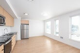 This single-floor space showcases a clean, contemporary design with light hardwood-style flooring that runs seamlessly throughout. A welcoming hallway with recessed lighting leads into the main living area, where multiple windows fitted with horizontal blinds allow generous natural light to fill the room and offer views of the surrounding neighborhood.

The open-concept kitchen is a standout feature, outfitted with flat-front light wood cabinetry, dark granite-style countertops, and a classic white subway tile backsplash. A full suite of stainless steel appliances includes a refrigerator, electric range, over-the-range microwave, and dishwasher, making the kitchen both functional and stylish. The layout flows naturally into the living space, making it well-suited for everyday living and entertaining.

The living area is generously proportioned, bright, and open, with a neutral white color palette that creates a calm, airy ambiance. Flush-mount ceiling fixtures provide consistent lighting throughout.

The bathroom is thoughtfully finished with a full soaking tub and shower combination, light wood-toned cabinetry with a dark countertop, and clean white walls that complement the rest of the unit's modern aesthetic. The overall design is cohesive, functional, and move-in ready.
