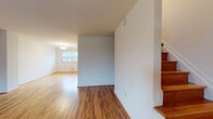 Located at 1114 Tace Drive in Essex, Maryland, this three-floor home offers a well-organized layout across its multiple levels. The main living area features warm, honey-toned hardwood flooring that extends throughout, complemented by clean white walls that create a bright and open atmosphere. A chandelier-lit space at the front of the home allows natural light to pour in through a large window, adding to the welcoming ambiance. The staircase, with its rich wood treads, serves as a central design element connecting all three floors.

The galley-style kitchen is efficiently designed with dark cabinetry, light countertops, and white appliances including a gas range and refrigerator. A windowed back door provides additional natural light and exterior access. Upstairs, the bedrooms continue the hardwood flooring theme, with one room featuring dual closets offering generous storage. A full bathroom on the upper level includes a tiled tub-shower combination, a dark-vanity with a white basin, and a window for natural ventilation.

The lower level presents an unfinished basement with painted concrete floors, exposed ceiling joists, and concrete block walls — offering significant potential for customization or additional storage. Stairways connecting all three levels are clearly defined, making the home easy to navigate throughout.