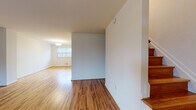 Located at 1114 Tace Drive in Essex, Maryland, this three-floor home offers a well-organized layout across its multiple levels. The main living area features warm, honey-toned hardwood flooring that extends throughout, complemented by clean white walls that create a bright and open atmosphere. A chandelier-lit space at the front of the home allows natural light to pour in through a large window, adding to the welcoming ambiance. The staircase, with its rich wood treads, serves as a central design element connecting all three floors.

The galley-style kitchen is efficiently designed with dark cabinetry, light countertops, and white appliances including a gas range and refrigerator. A windowed back door provides additional natural light and exterior access. Upstairs, the bedrooms continue the hardwood flooring theme, with one room featuring dual closets offering generous storage. A full bathroom on the upper level includes a tiled tub-shower combination, a dark-vanity with a white basin, and a window for natural ventilation.

The lower level presents an unfinished basement with painted concrete floors, exposed ceiling joists, and concrete block walls — offering significant potential for customization or additional storage. Stairways connecting all three levels are clearly defined, making the home easy to navigate throughout.
