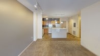 This single-floor unit offers a practical and comfortable layout designed for everyday living. The open-concept kitchen and living area serves as the heart of the space, where warm honey-oak cabinetry pairs with light countertops, a full suite of white appliances including a refrigerator, range, and dishwasher, and tile flooring in a stone-like pattern. Track lighting illuminates the kitchen, which features ample upper and lower cabinet storage and a double-basin sink. A central island with a white countertop provides additional workspace and visual separation from the carpeted living area. The living space is generously sized, with track lighting overhead and a set of glass patio doors that invite natural light and provide access to an outdoor area. An electrical panel and wall-mounted thermostat are conveniently located near the entry door. The two bedrooms are carpeted and bright, each featuring windows with blinds that frame outdoor views of surrounding greenery. The primary bathroom includes a walk-in shower with grab bars, a single-sink vanity with oak cabinetry, and tile flooring. The second bathroom offers a full soaking tub, a single-sink vanity, and matching tile flooring. Both bathrooms are finished with grab bars and medicine cabinets, lending a thoughtful, accessible design throughout.
