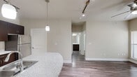 Located in Bee Cave, Texas, this single-story, one-bedroom, one-bathroom residence offers a thoughtfully designed layout that maximizes its compact footprint. The open-concept kitchen serves as the centerpiece of the living area, showcasing rich dark-brown cabinetry, granite-style stone countertops, a white subway tile backsplash, and a full suite of stainless steel appliances including an electric range, over-the-range microwave, and refrigerator. A curved peninsula with an integrated sink provides additional prep space and casual seating, illuminated by stylish pendant lights and a track lighting system overhead. Wood-look plank flooring flows throughout the main living areas, adding warmth and continuity to the space. The bedroom is carpeted for comfort and features a window fitted with white blinds that allow natural light to filter in. The full bathroom continues the cohesive design aesthetic with matching dark cabinetry, stone countertops, and wood-look flooring. A dedicated walk-in closet with built-in shelving and hanging rods adjoins the bedroom, offering generous storage. The in-unit laundry area houses a full-size washer and is equipped with overhead shelving for added convenience. Neutral wall tones throughout create a calm and versatile backdrop throughout the entire residence.