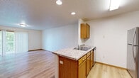 This one-bedroom, one-bathroom unit in Fargo, North Dakota offers a well-organized single-floor layout designed for comfortable everyday living. The open-concept kitchen serves as the heart of the home, featuring warm oak cabinetry, light granite-style countertops, a peninsula with a double sink, and a full suite of stainless steel appliances including a refrigerator, electric range, and over-the-range microwave. Light hardwood flooring runs throughout the kitchen and living areas, lending a clean, cohesive feel to the space. The living room is bright and spacious, highlighted by a sliding glass door with vertical blinds that invites natural light and provides access to an outdoor area. A baseboard heating system and wall-mounted air conditioning unit ensure year-round comfort. The bedroom is generously sized, finished with plush carpet, a window with outdoor views, and baseboard heat. The full bathroom includes tile flooring, a wood vanity with ample storage, and a well-lit mirror. A dedicated laundry room with a full-size washer and dryer adds everyday convenience. Textured ceilings and warm wood trim throughout tie the space together with a consistent, inviting aesthetic.
