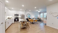 This single-story residence is designed with a clean, contemporary aesthetic that emphasizes open living and functional design. The heart of the home is a seamlessly connected kitchen, dining, and living area that creates a spacious, airy atmosphere. The kitchen is outfitted with white shaker-style cabinetry, a white subway tile backsplash, light quartz countertops, a full suite of stainless steel appliances including a refrigerator, range, microwave, and dishwasher, and a freestanding island that provides additional prep and casual dining space. Recessed lighting and under-cabinet illumination keep the area well-lit throughout the day.

The open-concept layout flows naturally into the dining and living areas, unified by light wood-style flooring and a neutral color palette. The living room benefits from natural light through large windows and is equipped with a ceiling fan. A full bathroom features white cabinetry, a quartz-topped vanity with an undermount sink, and a tub-shower combination. Both bedrooms offer carpeted flooring, ceiling fans, and generous natural light from multiple windows with blinds and sheer curtains. The overall ambiance is bright, clean, and welcoming throughout.