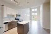 Located at 299 N Highland Ave in Atlanta's dynamic Old Fourth Ward, this thoughtfully designed one-bedroom, one-bathroom residence offers a bright and modern living experience. The open-concept layout is anchored by a striking kitchen featuring two-tone cabinetry — crisp white uppers paired with rich dark wood lowers — complemented by a light subway tile backsplash, stainless steel appliances including a refrigerator, range, microwave, and dishwasher, and a sleek central island with a white quartz countertop and pendant lighting above. Light wood-style flooring extends through the main living area, which impresses with dramatically soaring ceilings and clerestory windows that flood the space with natural light. A sliding glass door opens to a private balcony, offering views of the surrounding neighborhood. The bedroom is carpeted for comfort, benefits from tall ceilings, and features a large window with outdoor views. Two closets provide ample storage. The bathroom is finished with a dark wood vanity, white quartz countertop, a large mirror, and a glass-enclosed walk-in shower with tile flooring, maintaining the clean, contemporary aesthetic found throughout the home.