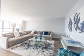 Located at 57 Widdicombe Hill Blvd in Toronto's west end, this 2-bedroom, 2-bathroom residence offers a thoughtfully designed single-floor layout with modern finishes throughout. The entryway is marked by a striking large-scale art piece that sets a contemporary tone as it opens into the living area, where warm wood-look flooring, neutral-toned walls, and ample space create a welcoming atmosphere. The living room features a comfortable seating arrangement and flows seamlessly toward expansive windows that frame city views. The kitchen is outfitted with high-gloss white cabinetry, a peninsula with counter seating, stainless steel appliances, and recessed lighting, connecting directly to the dining area where floor-to-ceiling windows provide abundant natural light and panoramic urban vistas. The generously sized primary bedroom includes large windows with city views, hardwood-style flooring, and direct access to a well-appointed ensuite bathroom featuring a double-sink vanity with undermount basins and clean white cabinetry. The second bedroom is equally spacious and bright, with its own access to the second full bathroom. A hallway connects all rooms efficiently, completing this refined and functional urban residence.