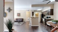 Located at 1456 Serfas Club Dr in Corona, California, this single-story residence at Del Oro Apartments offers a well-designed open-concept floor plan that seamlessly connects the main living areas. Rich, dark hardwood-style flooring flows throughout the living, dining, and kitchen spaces, creating a cohesive and contemporary aesthetic.

The kitchen is a functional centerpiece, featuring dark espresso cabinetry, granite-style countertops, a suite of stainless steel appliances including a refrigerator, microwave, and range, and a skylight overhead that floods the space with natural light. A breakfast bar with modern bar seating provides a casual dining option and visually connects the kitchen to the open living area.

The living room is highlighted by a tiled fireplace flanked by open shelving, with vertical blinds offering access to natural light. A dedicated dining nook accommodates a round table and chairs, ideal for everyday meals. The bedroom features plush carpeting, generous closet access, and a large sliding glass door with vertical blinds that invite in natural light.

The bathroom is finished with dark wood cabinetry, granite countertops, a single vanity sink, and a shower-tub combination. A ceiling fan is noted in the main living area, contributing to overall comfort throughout this thoughtfully appointed home.