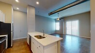 This single-floor unit showcases a compelling blend of industrial and contemporary design, defined by rich polished concrete floors that extend seamlessly throughout the entire space. The open-concept layout connects the kitchen and living areas, creating a flowing, expansive feel enhanced by soaring ceilings and exposed metallic ductwork that adds a distinctive industrial character.

The kitchen is a standout feature, equipped with crisp white shaker cabinetry reaching toward the ceiling, a classic subway tile backsplash, and a full suite of stainless steel appliances including a refrigerator, range, and microwave. A large central island with a quartz countertop and double-basin sink serves as both a functional workspace and a natural gathering point.

The open living area benefits from generous ceiling height, recessed lighting, and a ceiling fan, while wide sliding glass doors and large windows invite abundant natural light and offer outdoor access. The bedrooms are well-proportioned, each featuring concrete floors, ceiling fans, and multiple windows fitted with blinds for privacy and light control. Structural concrete columns punctuate the space, reinforcing its urban loft aesthetic.

The bathroom is cleanly finished with white subway tile in a walk-in shower with a glass door, a white vanity, and consistent concrete flooring, maintaining the cohesive industrial-modern design found throughout the unit.