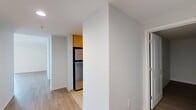 This single-floor, 2-bedroom, 1-bathroom unit offers a clean, modern layout designed for comfortable everyday living. The interior is finished with light wood-tone flooring throughout the main living areas and hallways, contributing to a bright, cohesive aesthetic. The living room is a generously proportioned open space featuring sliding glass doors that lead to a private balcony, filling the room with natural light and providing outdoor views of the surrounding cityscape. The galley-style kitchen is efficiently designed with warm wood cabinetry on both sides, dark granite-style countertops, light tile flooring, and a full suite of stainless steel appliances including a refrigerator, oven, and dishwasher, all illuminated by a central flush-mount ceiling fixture. The primary bedroom is a well-sized room featuring large windows that frame urban views and allow ample natural light to enter. The second bedroom offers a more intimate space with darker hardwood-style flooring and a built-in closet with panel doors. The bathroom is finished with light tile flooring and includes a full soaking tub with a shower surround. Multiple hallways connect the various rooms, creating a logical and functional flow throughout the unit. Neutral wall tones and clean lines give the space a move-in-ready, contemporary feel.