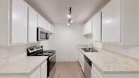 Located at 4456 W 238th St in Torrance, California, this single-floor unit offers a clean, neutral interior designed for comfortable everyday living. The open living area is generously proportioned, finished with plush wall-to-wall carpeting and crisp white walls that lend a bright, airy feel. A large sliding glass door fitted with vertical blinds allows natural light to fill the space while providing access to the outdoors.

The galley-style kitchen is thoughtfully laid out with white cabinetry lining both sides, light-toned laminate countertops, and wood-style flooring. It is equipped with a stainless electric range, built-in microwave, dishwasher, and a double-basin sink. Track lighting overhead ensures the space is well illuminated. A peninsula counter connects the kitchen to the adjoining living and dining area.

A hallway leads from the main living space to the bedroom, which features carpeted flooring, a window with vertical blinds that brings in natural light, and a baseboard heating system. The bathroom includes a tub and shower combination enclosed by sliding glass doors with chrome hardware. Baseboard heating is also present in the living areas, and a ceiling fan adds comfort to additional spaces within the unit.