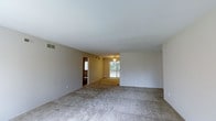 This upgraded 2-bedroom, 2-bathroom single-floor residence offers a well-designed, open layout that maximizes living space throughout. The living area is generously sized, featuring neutral-toned carpet, smooth ceilings, and a ceiling fan with integrated lighting. A sliding glass door floods the space with natural light while providing direct access to an outdoor area, enhancing the sense of openness.

The kitchen is positioned adjacent to the living space in an open-concept arrangement, featuring warm oak cabinetry, light stone-toned countertops, and black appliances including a refrigerator, range, and built-in microwave. The kitchen floor transitions to wood-style flooring, clearly delineating it from the carpeted living area. A ceiling fan overhead adds both function and visual continuity with the main living space.

The neutral, light gray wall tones carry throughout the unit, creating a cohesive and calming ambiance. Ample electrical outlets and ceiling vents are thoughtfully placed throughout for comfort and convenience. The overall design balances practicality with an upgraded aesthetic, making this a comfortable and move-in ready space.