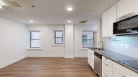 Located at 3845 Main St in Kansas City, MO, this efficiently designed studio unit offers a thoughtfully organized single-floor layout. The open living area features warm wood-look flooring, crisp white walls, and recessed lighting complemented by a ceiling fan, creating a bright and clean atmosphere. Two framed windows allow natural light to filter in, offering views of the surrounding brick building exterior.

The kitchen is sleek and modern, finished with flat-front white cabinetry extending to the ceiling for ample storage. Stainless steel appliances include a full-size refrigerator, over-the-range microwave, dishwasher, and a cooktop, all paired with gray countertops and a tile backsplash with under-cabinet lighting. The kitchen flows seamlessly into the living space, making the layout feel open and functional.

The bathroom is clean and minimalist, featuring all-white finishes, a soaking tub with an overhead shower, chrome fixtures, and wood-look flooring that ties back to the rest of the unit. The space as a whole presents a contemporary, move-in-ready aesthetic well-suited for urban living in the heart of Kansas City.