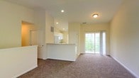 Located at 3900 Suffolk Dr in Dublin, Ohio, this single-floor residence offers a well-designed open-concept layout that maximizes both functionality and comfort. The living area is generously proportioned, featuring plush wall-to-wall carpeting and vaulted ceilings that lend an airy, open feel to the space. Recessed lighting illuminates the interior, complemented by natural light streaming in through a large sliding glass door that provides direct access to the outdoors and offers views of surrounding greenery.

The kitchen is seamlessly integrated into the main living space via a peninsula-style breakfast bar, creating a natural transition between cooking and entertaining areas. It is outfitted with white cabinetry, including upper cabinets that extend toward the ceiling for ample storage. A full-size refrigerator, dishwasher, and a double-basin stainless steel sink round out the kitchen's practical amenities. Neutral-toned countertops and a ventilation vent overhead complete the efficient layout.

Throughout the home, warm beige and cream tones on the walls create a bright, welcoming atmosphere. The single-floor design ensures easy accessibility and a cohesive flow between all areas of the residence, making it a practical and comfortable living space in the Dublin, Ohio community.
