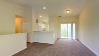Located at 3900 Suffolk Dr in Dublin, Ohio, this single-floor residence offers a well-designed open-concept layout that maximizes both functionality and comfort. The living area is generously proportioned, featuring plush wall-to-wall carpeting and vaulted ceilings that lend an airy, open feel to the space. Recessed lighting illuminates the interior, complemented by natural light streaming in through a large sliding glass door that provides direct access to the outdoors and offers views of surrounding greenery.

The kitchen is seamlessly integrated into the main living space via a peninsula-style breakfast bar, creating a natural transition between cooking and entertaining areas. It is outfitted with white cabinetry, including upper cabinets that extend toward the ceiling for ample storage. A full-size refrigerator, dishwasher, and a double-basin stainless steel sink round out the kitchen's practical amenities. Neutral-toned countertops and a ventilation vent overhead complete the efficient layout.

Throughout the home, warm beige and cream tones on the walls create a bright, welcoming atmosphere. The single-floor design ensures easy accessibility and a cohesive flow between all areas of the residence, making it a practical and comfortable living space in the Dublin, Ohio community.